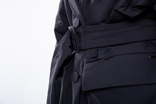 A close-up shot of a techwear coat with multiple pockets and straps, showcasing its functional and futuristic design.