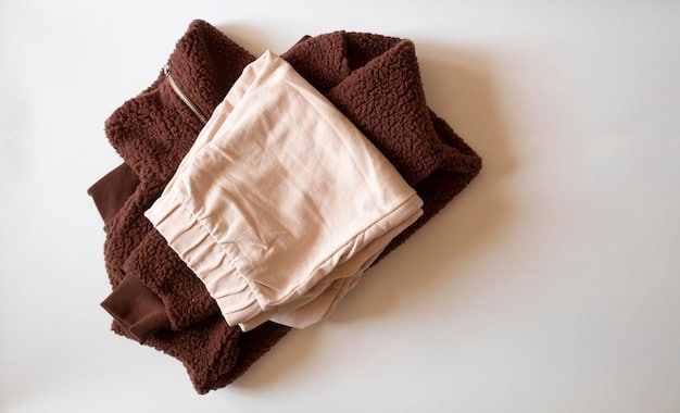 A close-up shot of a collection of neatly folded essential streetwear pieces, including plain white t-shirts, a black hoodie, dark wash jeans, and a grey sweatshirt. The background is a clean, minimalist wardrobe.