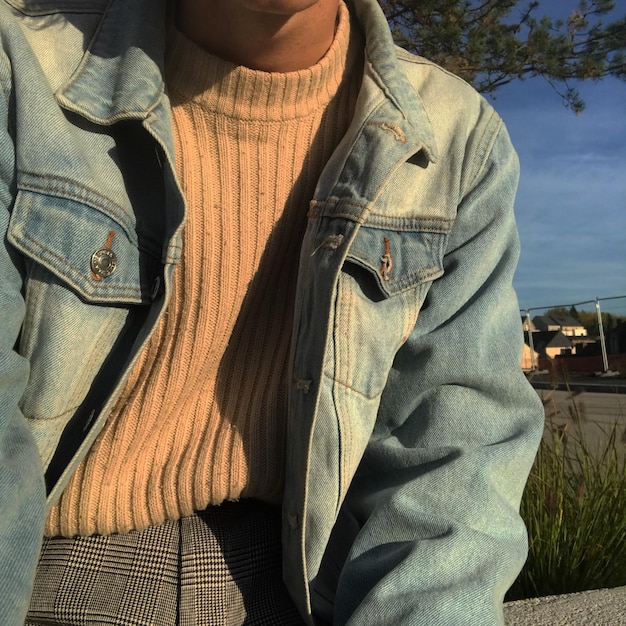 A man wearing a layered streetwear outfit in neutral tones, showcasing how different textures like denim, knitwear, and nylon can be combined to create a cohesive and stylish look.