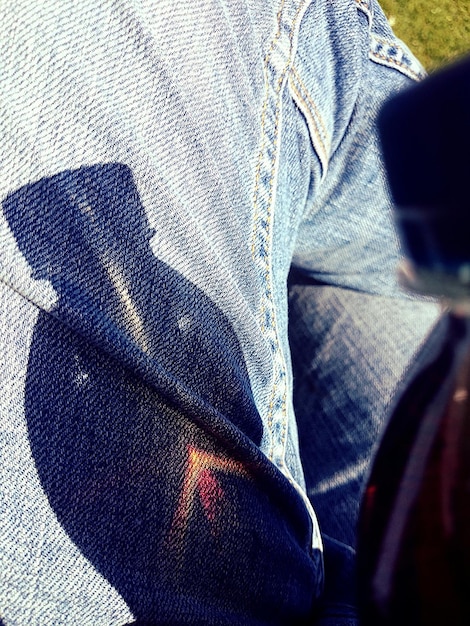 A close-up shot of a pair of dark wash, slightly distressed baggy jeans. The jeans are cuffed at the bottom to reveal a pair of high-top sneakers. The focus is on the texture of the denim and the details of the cuff.