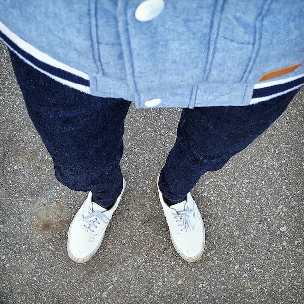 A close-up shot of a man's legs and feet, showcasing well-fitted jeans and stylish sneakers. The jeans have a slight taper, and the sneakers are a popular streetwear brand.