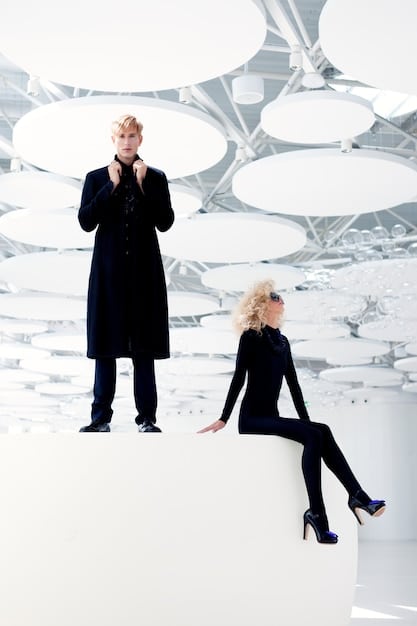 A high-fashion runway shot showcasing a collaboration between a luxury brand and a streetwear brand. The clothing should feature a blend of high-end tailoring and streetwear elements like hoodies, sneakers, and bold logos.