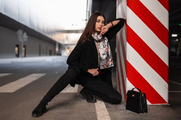 A model wearing an oversized black cashmere hoodie paired with tailored wide-leg trousers and black heeled boots. She is carrying a structured designer handbag and wearing gold hoop earrings.