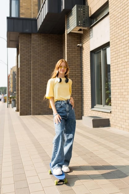 A young woman confidently walking down a city street, wearing light wash baggy jeans, a black crop top, and a vibrant oversized bomber jacket. She completes the look with white chunky sneakers and a small backpack.