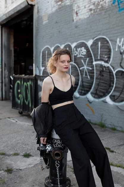 A woman wearing extremely oversized, baggy cargo pants with a cropped top and chunky sneakers, posing in a graffiti-covered alley.
