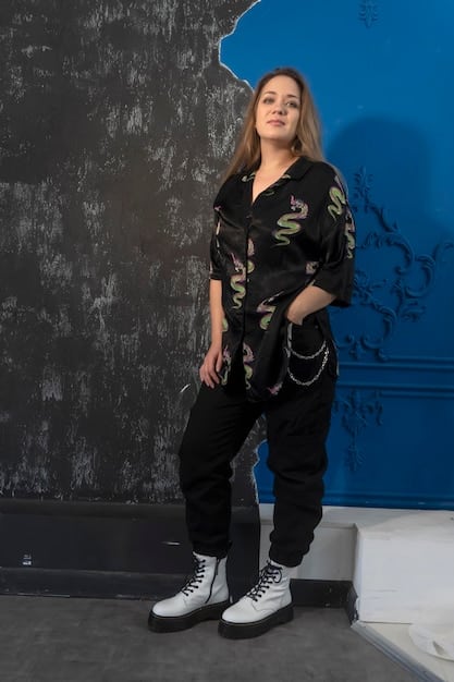 A fashionable woman wearing slim-fit black cargo pants with a graphic tee, an oversized denim jacket, and high-top sneakers, posing in front of a brick wall.