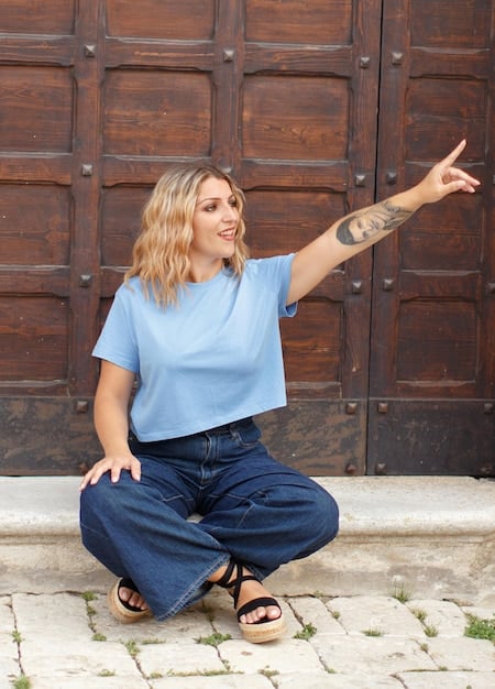 A plus-size model confidently wearing a stylish streetwear outfit, including a graphic tee, joggers, and sneakers. The model is smiling and posing in a natural, urban setting.