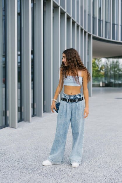 A woman standing on a sunny street wearing wide-leg trousers and a crop top, paired with chunky platform sandals. The focus is on the sandals, highlighting their bold style and how they complement the overall relaxed streetwear vibe.