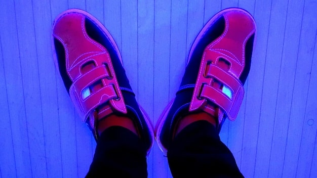 A close-up shot of a pair of retro-futuristic sneakers, highlighting the neon accents, asymmetrical design, and exaggerated sole. The background is blurred to focus on the intricate details of the sneakers.