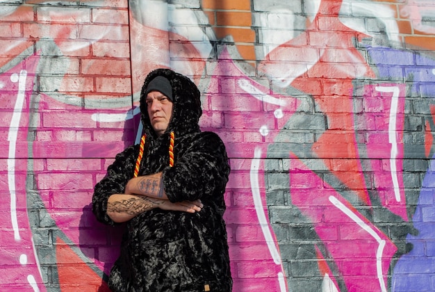 A person standing against a graffiti wall, wearing a colorful, printed puffer jacket with a unique design. The jacket is slightly cropped and paired with high-waisted jeans and chunky sneakers, showcasing an edgy urban look.