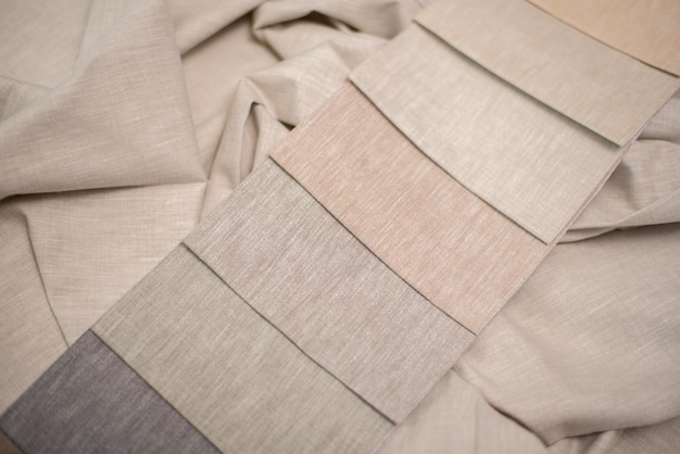 A close-up shot of various fabric swatches in different shades of beige and cream. The textures include knit, linen, and suede, showcasing the variety within a monochromatic palette.