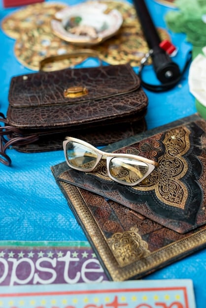 A close-up of various vintage accessories, including a classic leather handbag, a pair of cat-eye sunglasses, and a collection of vintage brooches displayed on a velvet cushion.