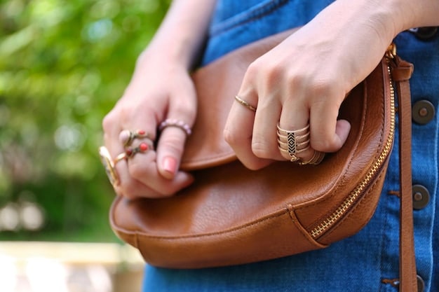 A close-up shot of a stylish woman's hands adjusting a small, vibrant orange utility-style crossbody bag over a neutral-colored oversized hoodie. Her nails are neatly done, adding a touch of personal flair.
