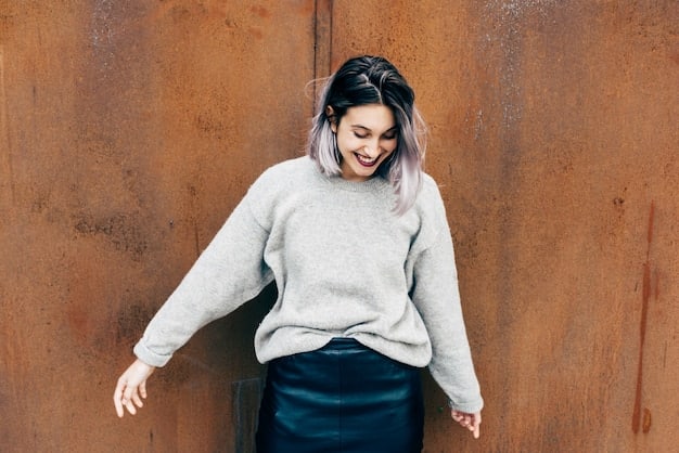 A woman posing in a chic setting, wearing an oversized heather grey hoodie, a flowing black silk slip skirt, and elegant white ankle boots. Her hair is casually styled, and she carries a sleek, minimalist clutch bag, blending comfort with refined style.