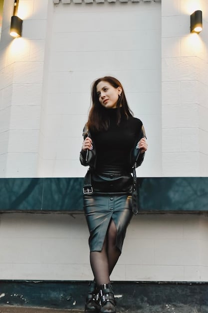 A woman wearing an oversized black hoodie, a black faux leather mini skirt, and chunky combat boots, with a dark, moody urban backdrop.