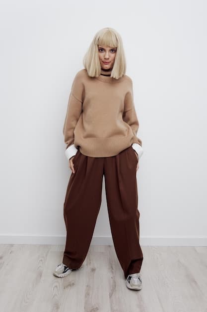 A woman wearing a layered outfit: a white long-sleeve tee peeking out from under a grey oversized hoodie, paired with beige wide-leg pants and a structured blazer draped over her shoulders.